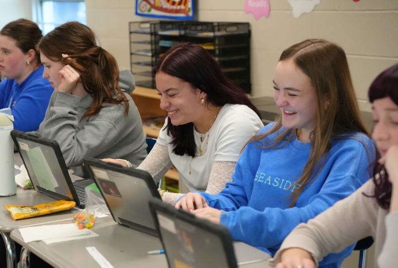 students laugh together as they work on a project on their laptops